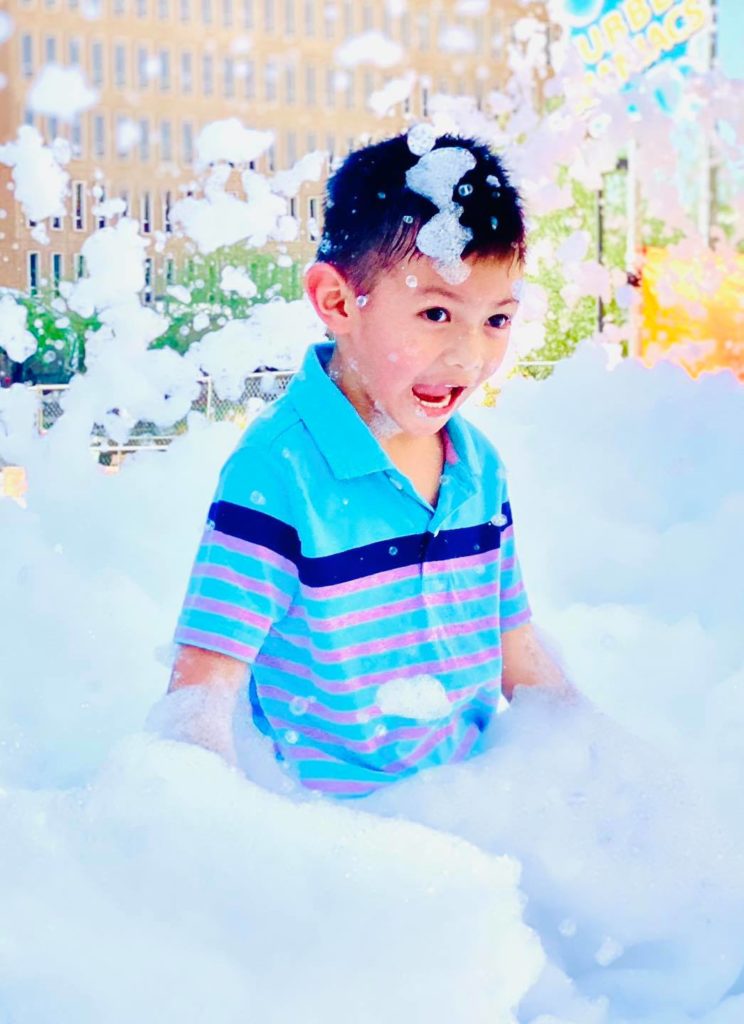 A boy laughing with bubbles on his head